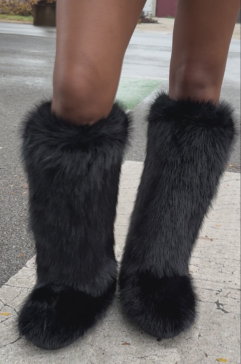 A video of a person posing outdoors on a wet urban street, wearing a textured black mini skirt and the AZALEA WANG EMIR BLACK FLAT FUR KNEE HIGH BOOT with bare legs.