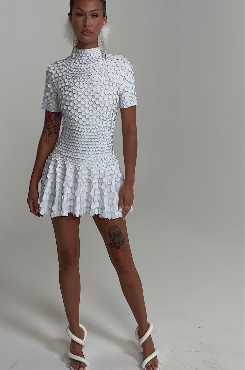 A video of a person in the FAR FROM BASIC SEQUIN MINI DRESS IN WHITE with hoop earrings and white high-heeled sandals.