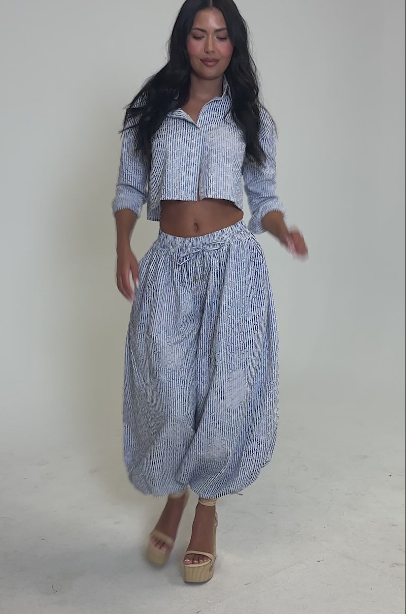 Video of woman modeling the BLOSSOM CROP BUTTON DOWN—a blue and white striped, cropped shirt—paired with matching high-waisted, loose pants.