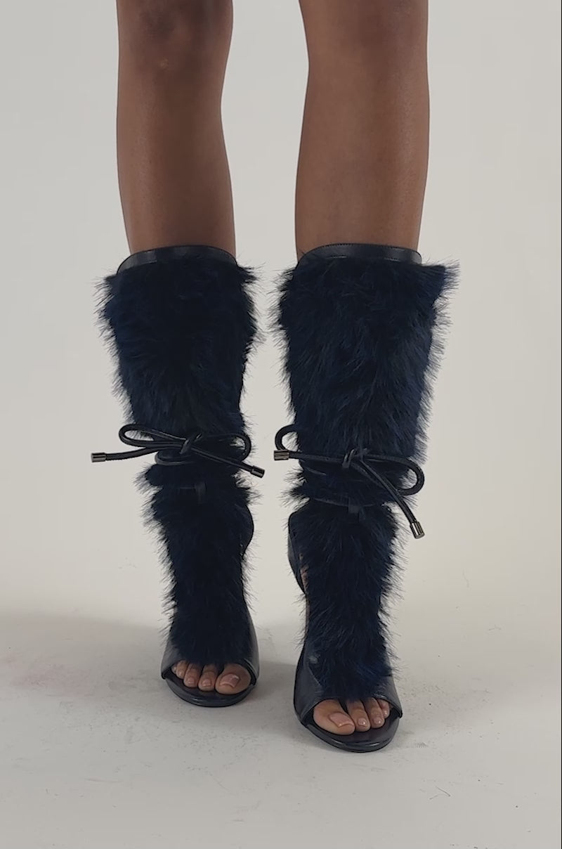 Video of a woman modeling the AZALEA WANG GENOVEVA NAVY FUR WEDGE SANDAL—open-toe wedge boots featuring dark blue fur trim and leather accents with lace-up details. 