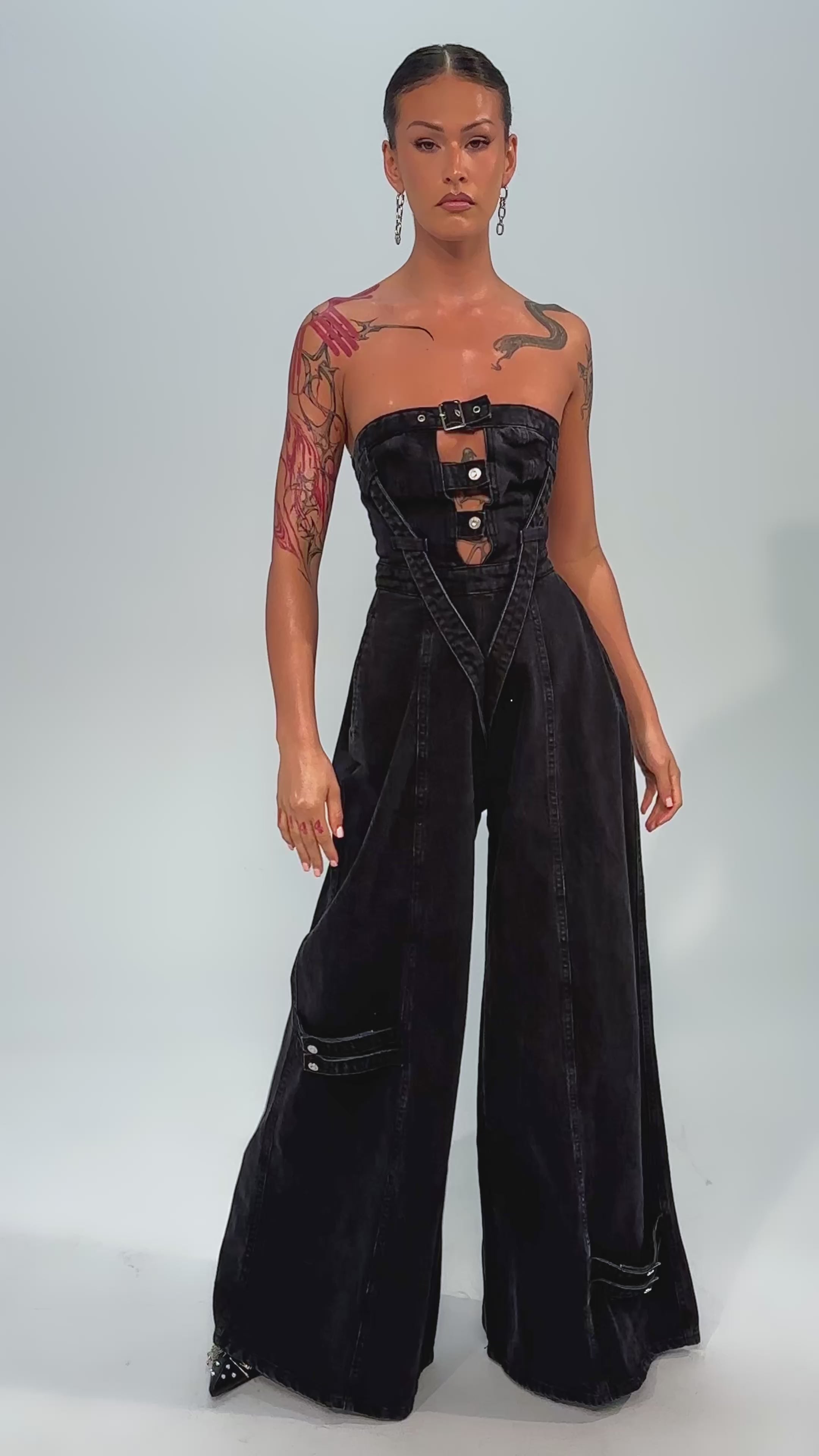 Video of woman modeling the SO YESTERDAY WIDE LEG DENIM JUMPSUIT, featuring a strapless black design, wide legs, and button details, against a plain light background.