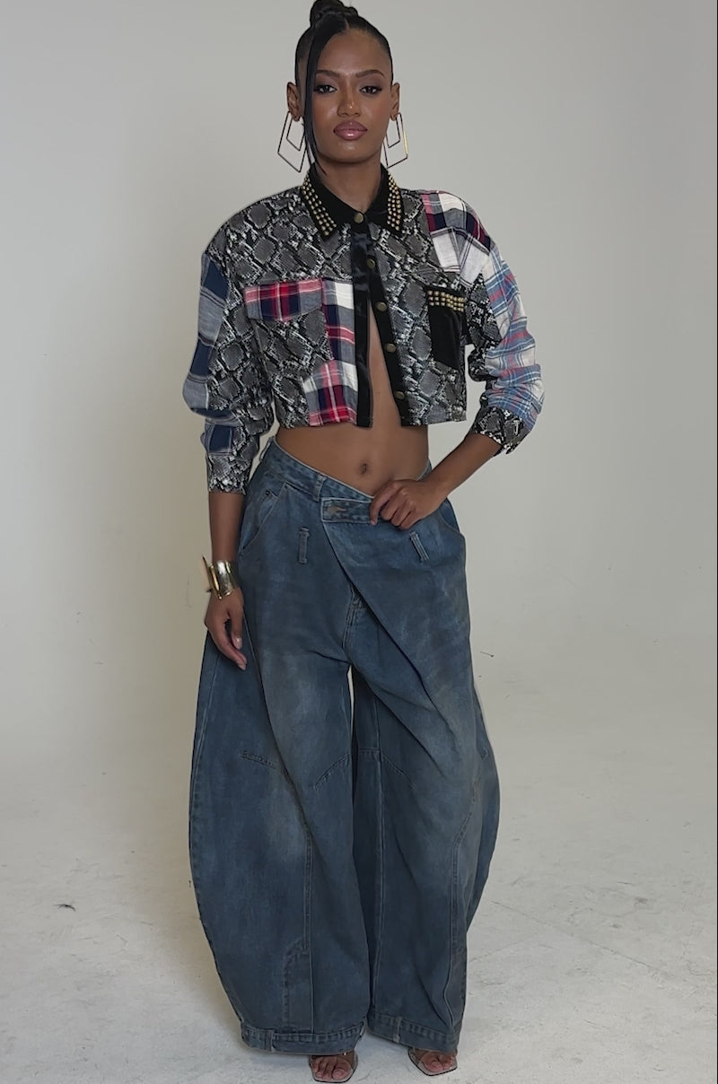 Video of woman modeling the GUESS WHATS NEXT PLAID BUTTON DOWN, styled as a cropped fit with plaid and snakeskin print accents plus studded details, paired with high-waisted wide-leg denim and gold hoop earrings