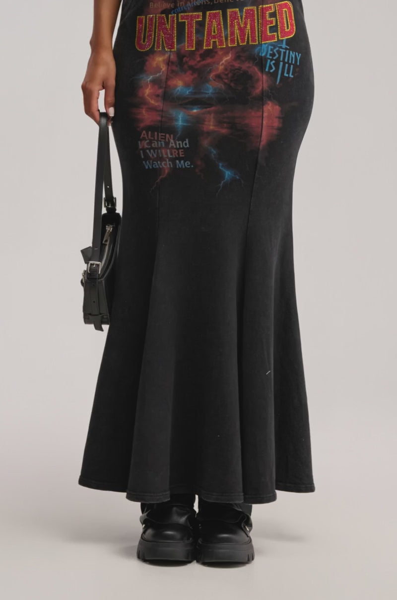 A video of a person wearing the UNTAMED FISHTAIL SKIRT, a black graphic midi with bold red "UNTAMED" text and lightning motifs, paired with black shoes and a small black bag for an edgy-chic vibe.