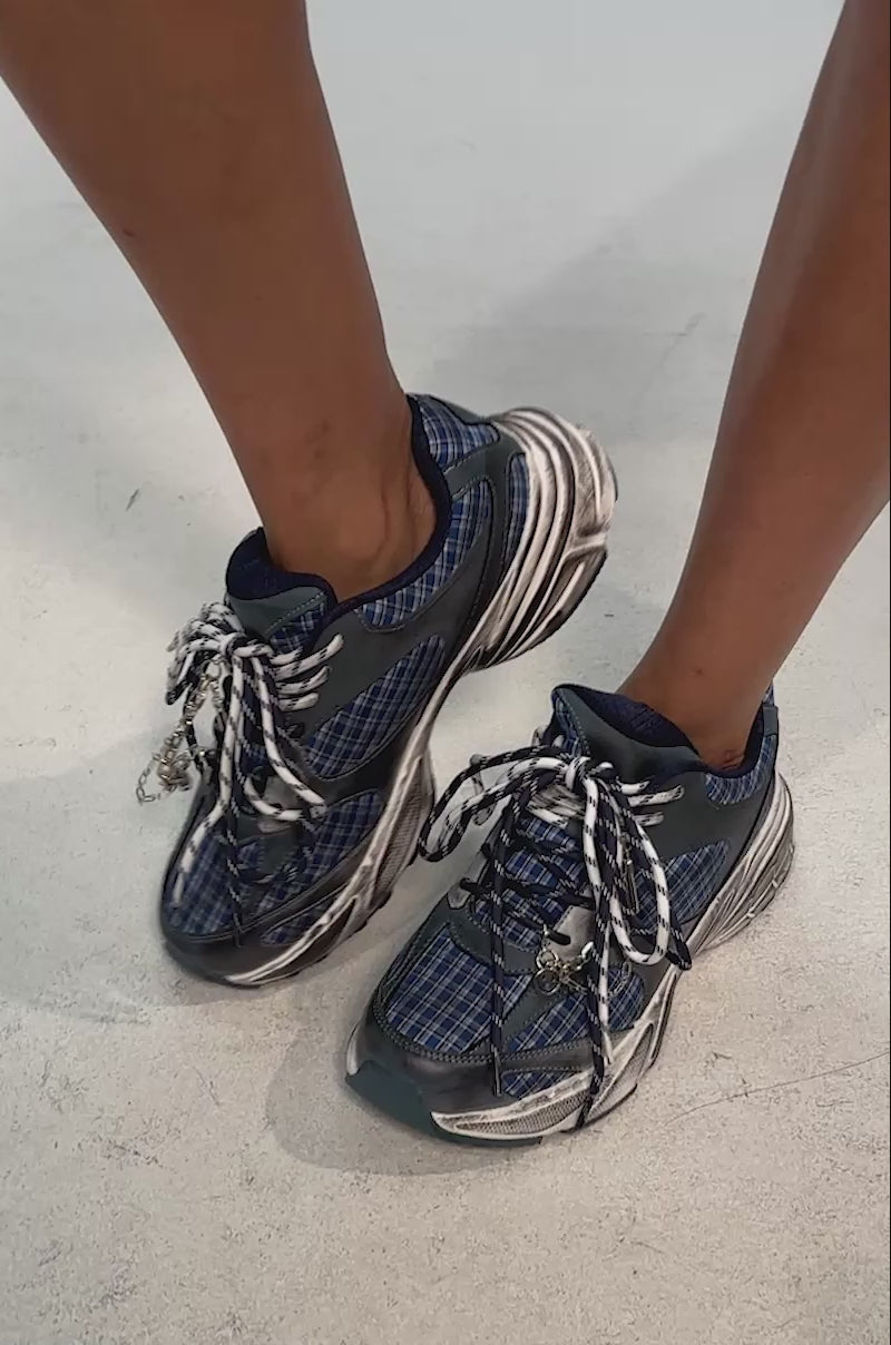 Video of woman modeling the AKIRA GOLD NOXA PLAID SILVER HARDWARE EMBELLISHED SNEAKER, set against a plain light background.