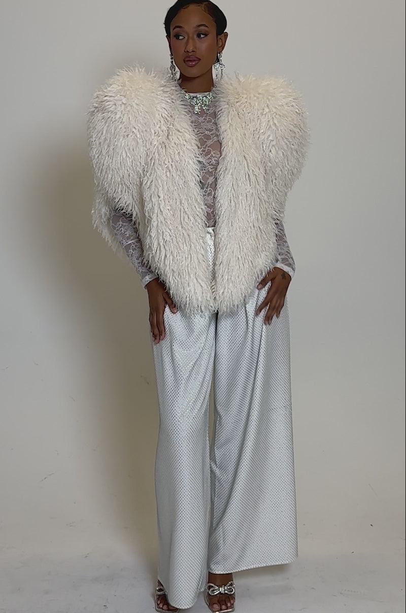 Video of woman modeling the STAR CROSSED LOVER FAUX FUR VEST IN IVORY over a lace top and high-waisted, wide-leg pants, standing against a plain background.
