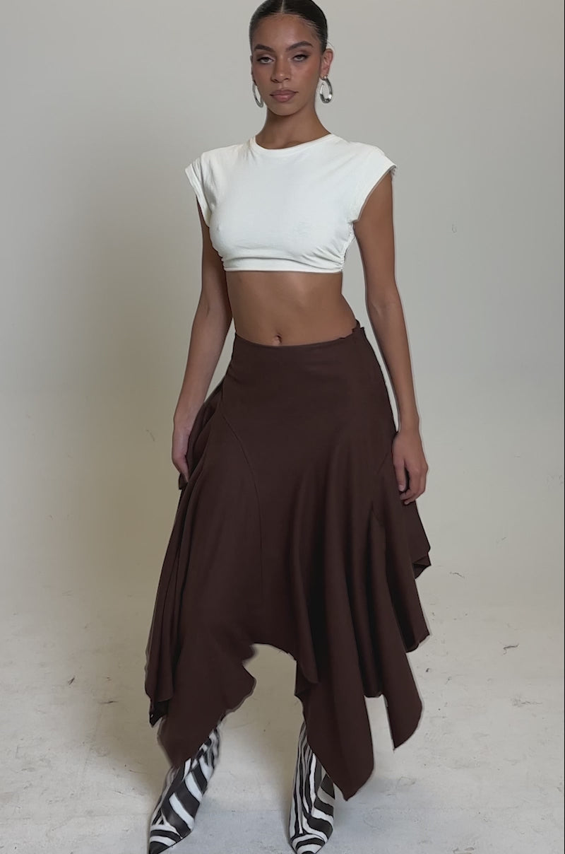 A video of a woman in a white cropped top, the FEELS GOOD MIDI SKIRT with a chunky white belt, and zebra-print knee-high boots against a plain light background.