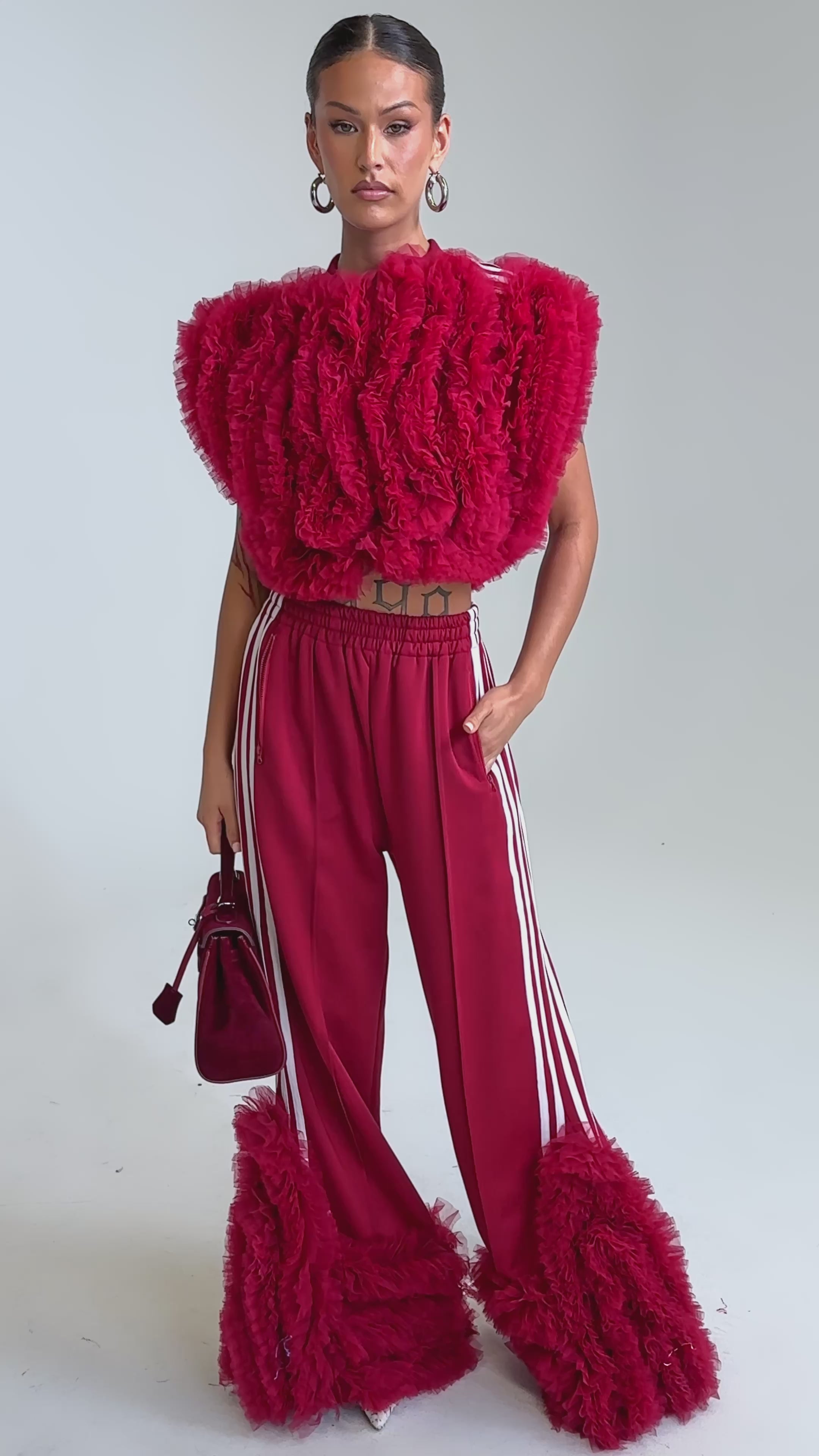 Video of woman modeling the MODERN JAM SWEATSHIRT WITH TULLE IN BURGUNDY, paired with bold red track pants featuring white stripes.