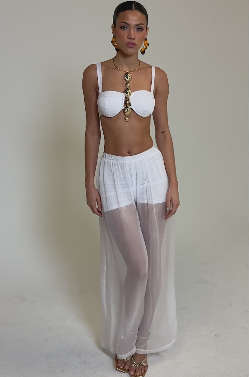 Video of woman modeling the DREAMY BRALETTE, sheer white high-waisted pants, bold drop earrings, and a statement gold necklace as she poses confidently against a neutral background.