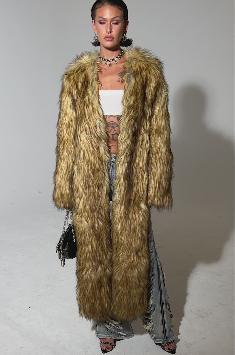 A video of a model wearing the LANGON HIGH LOW BOLERO over a white bandeau top and ripped jeans, accessorized with jewelry and a small handbag, a confident individual poses against a plain background.