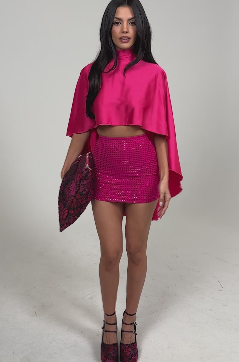 Video of woman modeling the MAKE A MOVE BLOUSE IN FUCHSIA, a vibrant satin top with a high neck and back tie detail, paired with a matching sequined mini skirt, posing confidently against a plain background.