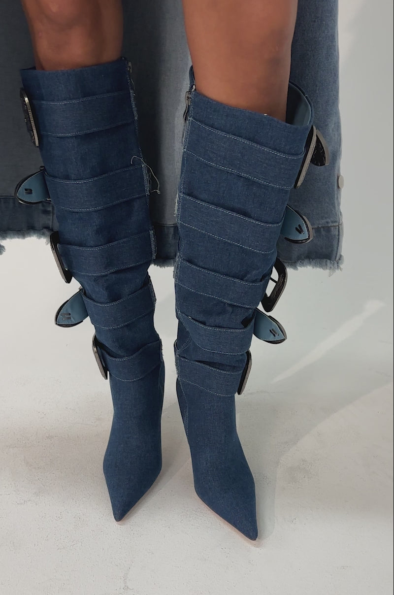 Video of woman modeling the AKIRA GOLD FALLON DENIM BUCKLE EMBELLISHED STILETTO BOOTS with bold buckles, standing against a plain light background.