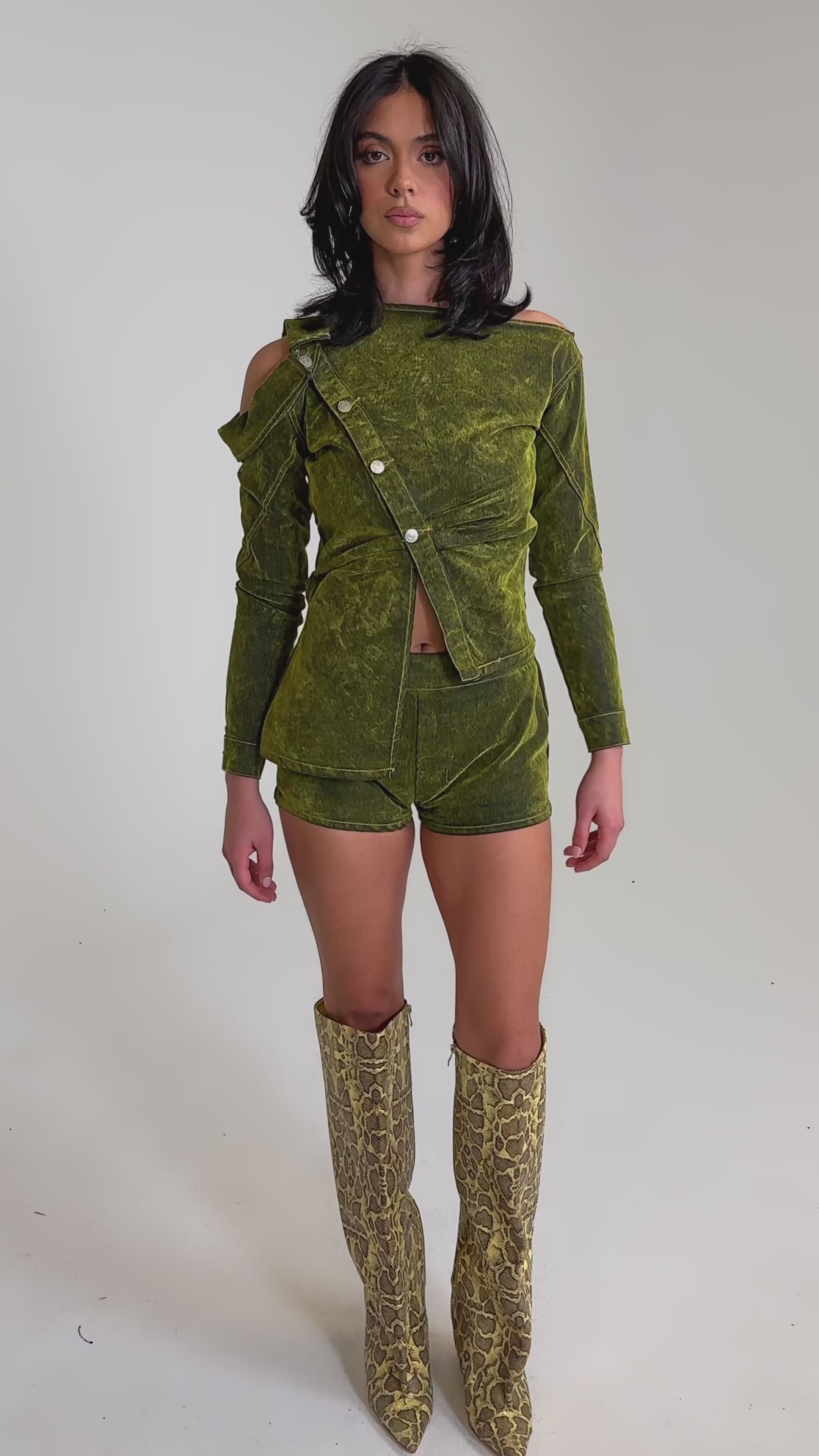 A video of a woman wearing the YOUR TIME IS COMING VELVET DENIM BLOUSE in green, paired with matching shorts and knee-high snake-print boots.