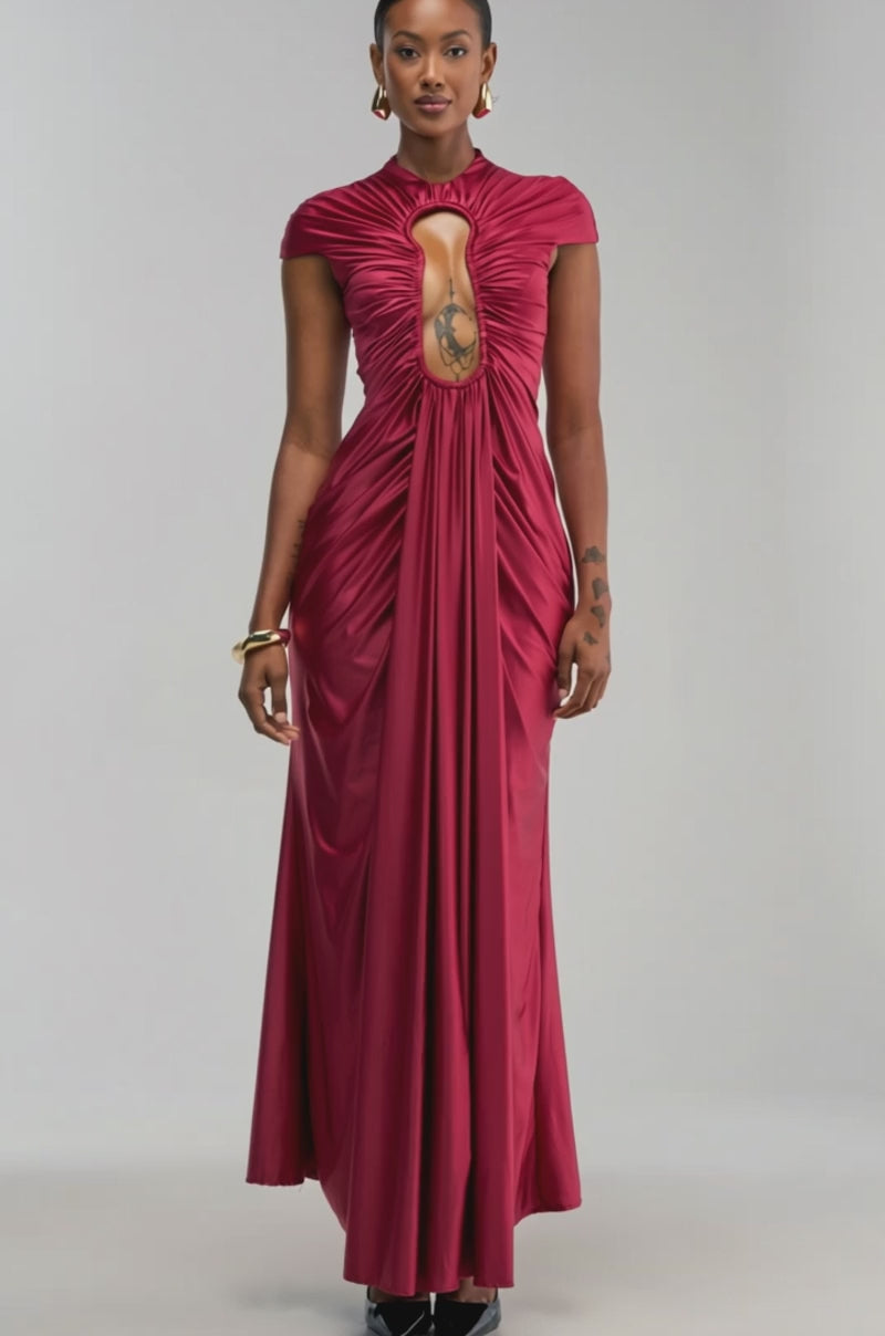 Video of a woman modeling the KEY TO MY HEART MAXI DRESS IN BURGUNDY poses in an elegant room adorned with candles, a chandelier, and a large mirror that reflects the back of her dress’s keyhole cutout. 