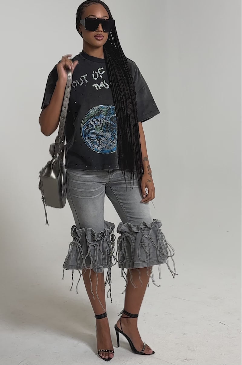 A video of a woman wearing sunglasses, a black graphic tee, strappy heels, a textured shoulder bag, and the JUMP ON IT DENIM BERMUDA SHORT.