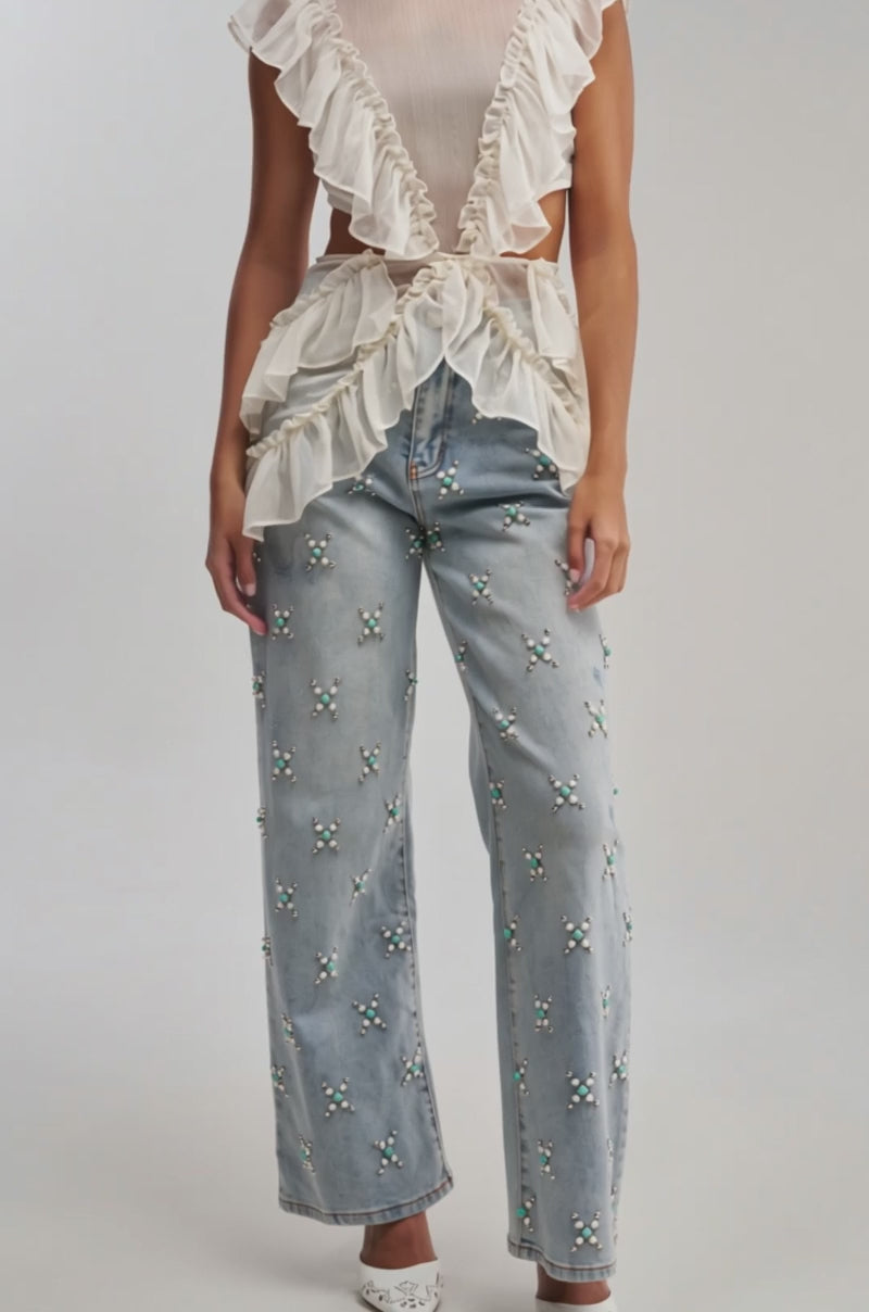 Video of woman modeling the TRYING SOMETHING OUT STUDDED DENIM—light blue wide-leg jeans embellished with pearl and bead clusters—and white pointed-toe shoes. 