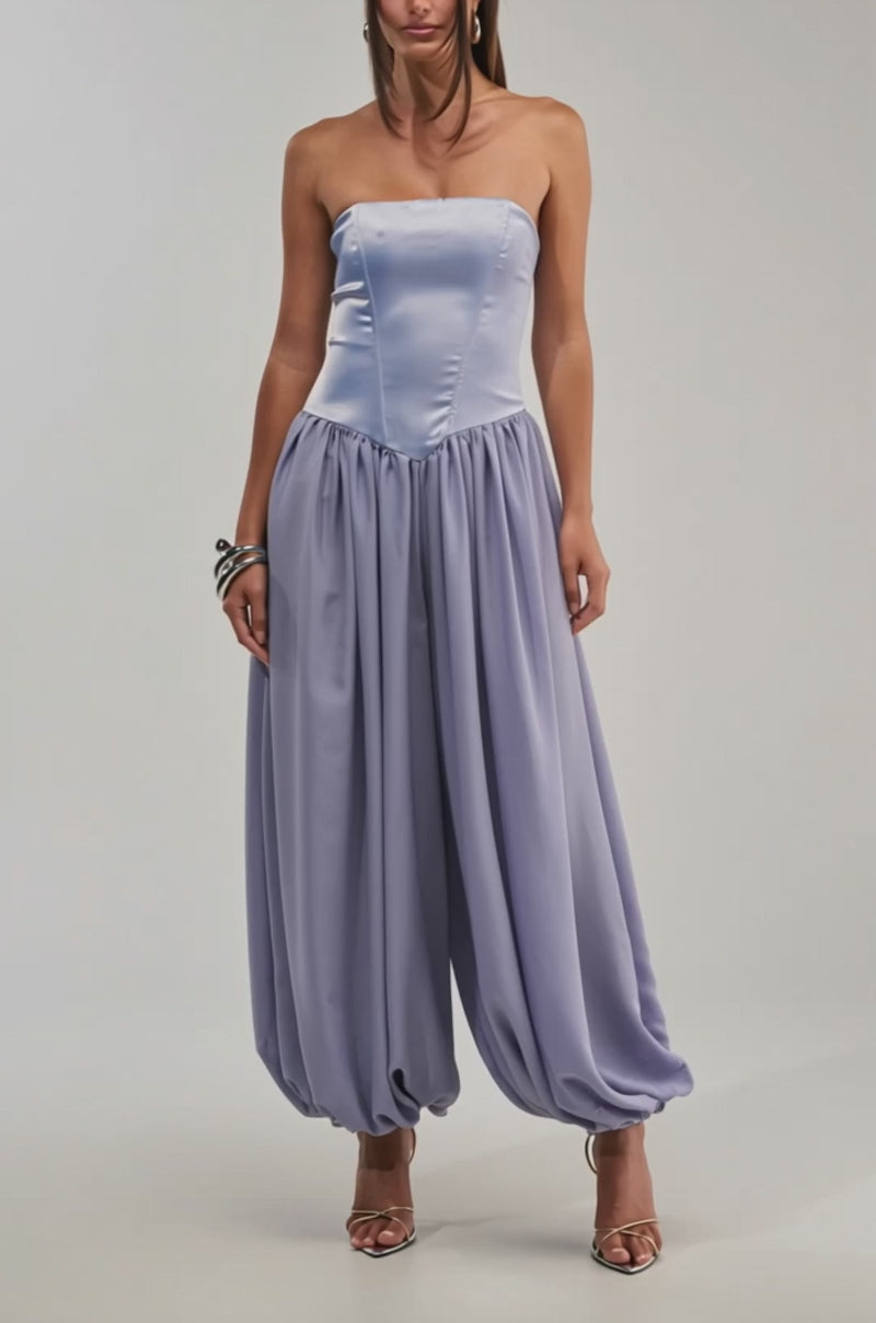 A video of a woman in the READ MY MIND STRAPLESS JUMPSUIT IN BLUE, featuring a fitted bodice and balloon-style pants, paired with strappy heels against a plain light background.