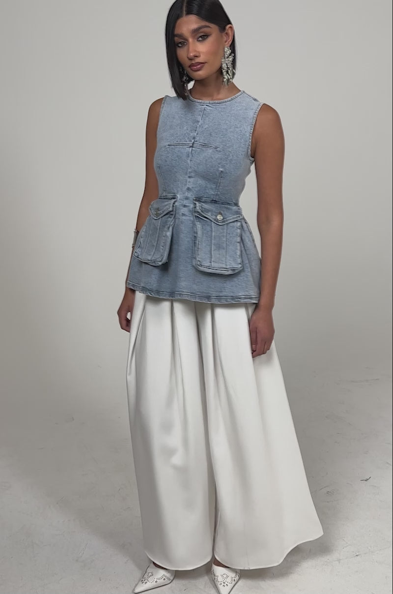 A video of a woman wearing the TURN AROUND DENIM BLOUSE, styled with wide-leg white trousers, white pointed shoes, and bold silver jewelry.