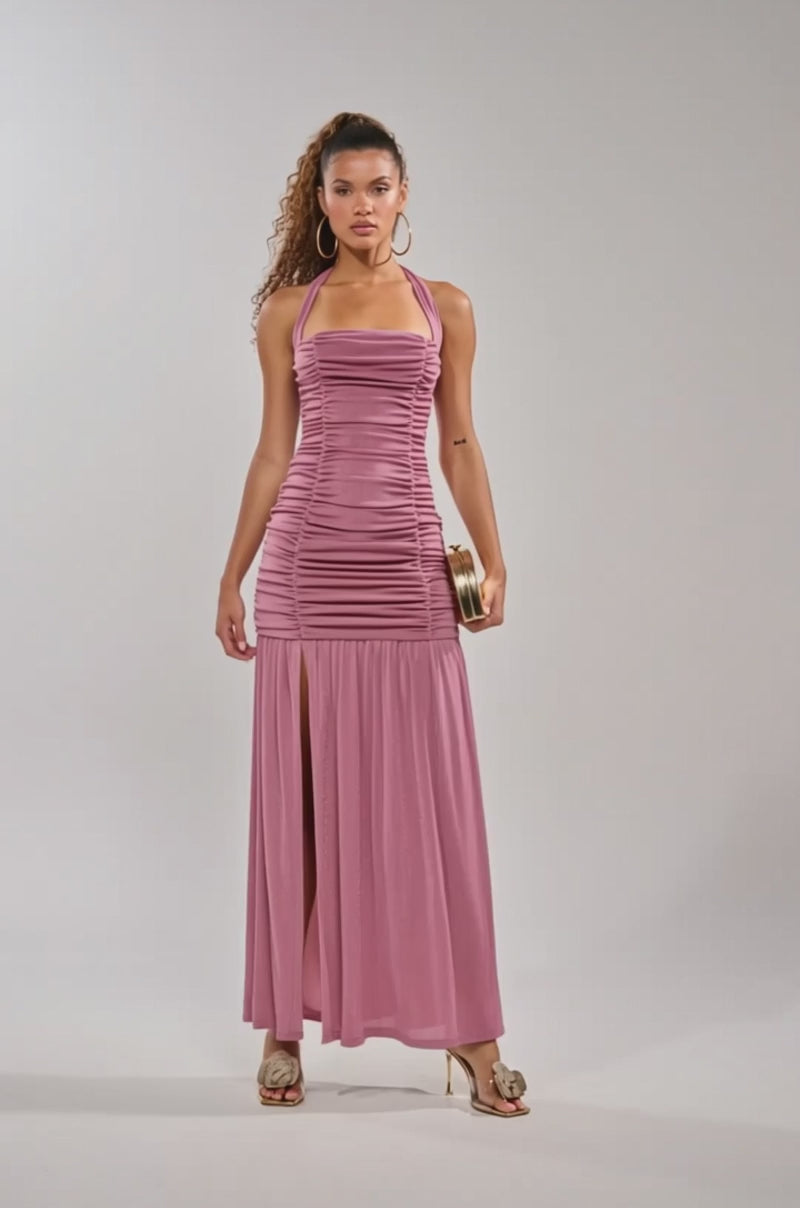 Video of woman modeling the NOTHING SUBTLE ABOUT IT RUCHED MAXI DRESS IN MAUVE, a sleeveless mesh maxi dress with a bodycon mermaid silhouette and thigh-high slit, styled with hoop earrings, heeled sandals, and a gold clutch.
