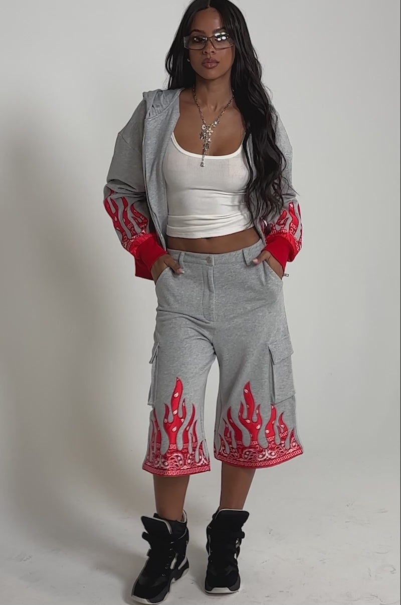 Video of woman modeling the FIRE TO THE FLAMES SWEATSHIRT—a gray zip-up with embroidered flames and bandana designs—matching sweatpants, glasses, and a necklace.