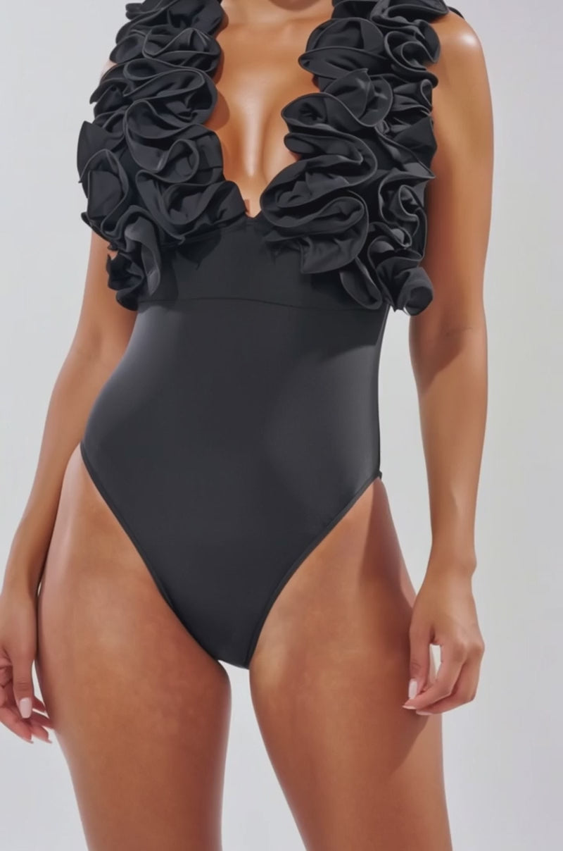 Video of woman modeling the FEEL MY POWER SWIMSUIT featuring a sculpting fit and dramatic ruffled details along the deep V neckline and shoulders.