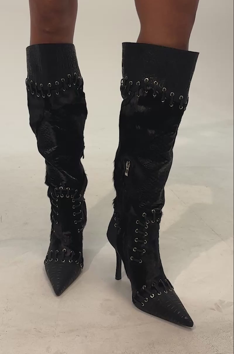 Video of woman modeling the AZALEA WANG NOVAK Black Pony Hair and Lace Up Stiletto Boot, featuring knee-high mixed textures of sleek black croc faux leather with silver eyelet details