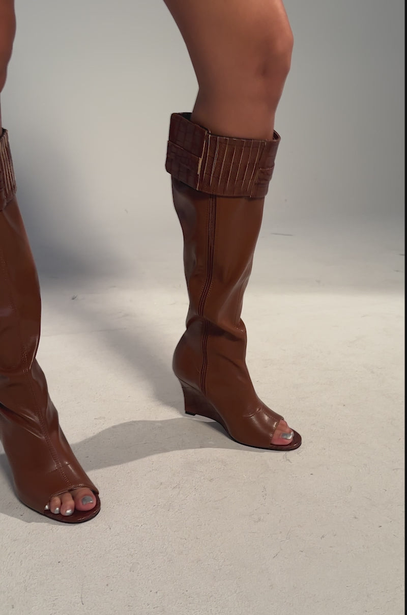A video of a person wearing AZALEA WANG GLENNA COGNAC STRETCH PU WEDGE BOOTS with cuffed tops and gold zipper detail. 