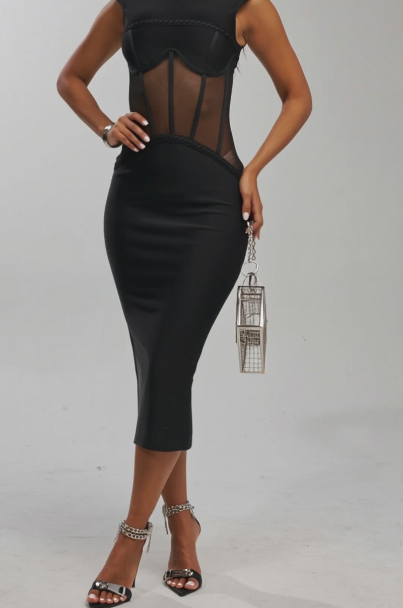 Video of woman modeling the ICONIC INSTINCT BANDAGE CORSET MIDI DRESS—sleek and black with sheer mesh panels—holding a geometric metallic handbag, wearing strappy heels, her long wavy dark hair styled loosely against a light background.
