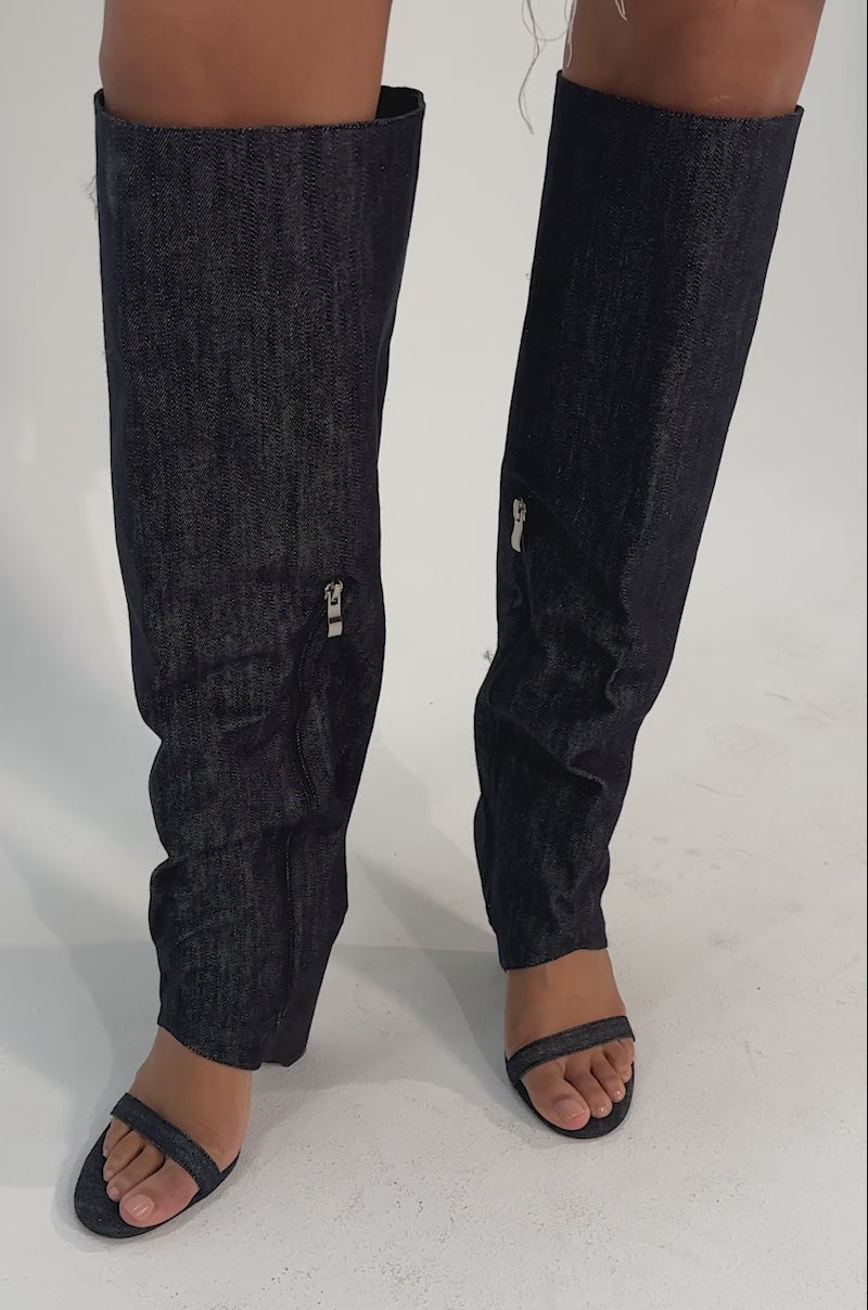A video of a person wearing the AZALEA WANG VEONA DARK DENIM OVER THE KNEE CHUNKY HEEL SANDALS with open toes and heels, standing against a plain background.