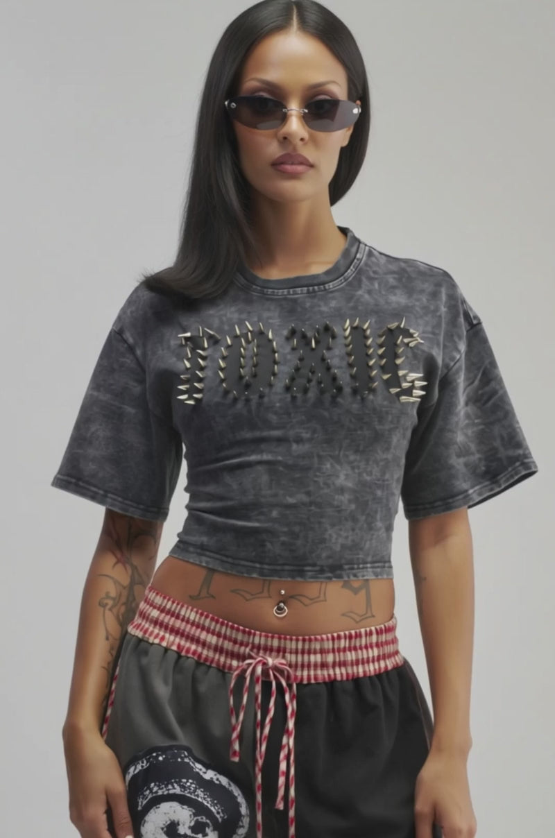 Video of a a woman modeling the TOXIC MINERAL WASH CROPPED TEE, which features “TOXIC” spelled out in spikes. 