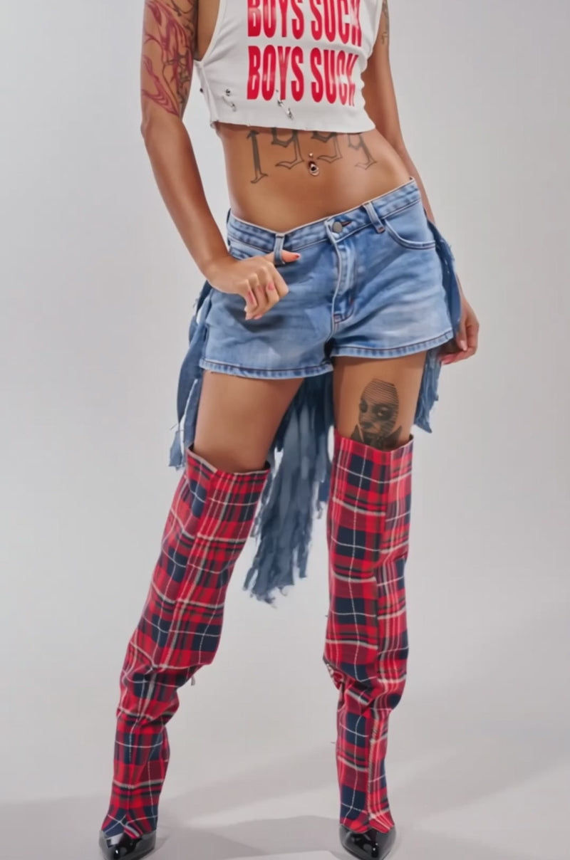 Video of woman modeling the TURN AROUND DISTRESSED DENIM SHORTS with frayed sides and red plaid thigh-high boots. 