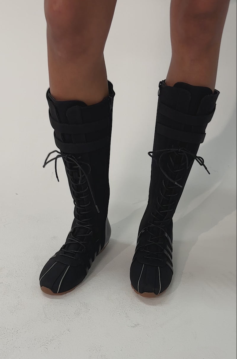 Video of woman modeling the AZALEA WANG OZZY BLACK FLAT SNEAKER—black, knee-high sneaker boots with lace-up fronts, Velcro straps, and brown soles