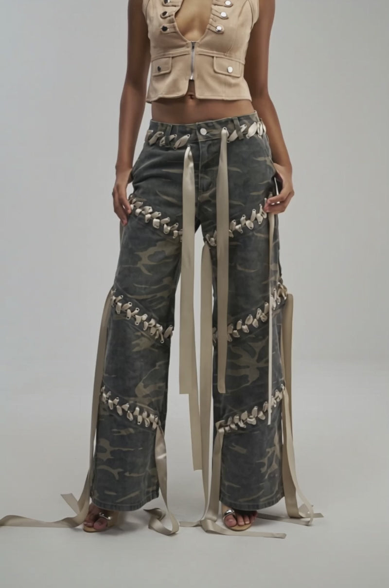 Video of a woman modeling the DOWN FOR SOME FUN CAMO PANT—wide leg camo pants decorated with beige ribbons.