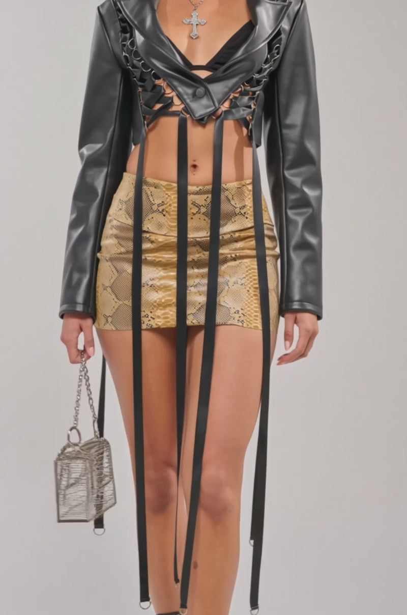 A video of a woman in the IN THE MOMENT LACE UP BLAZER, paired with a gold snakeskin mini skirt, hoop earrings, a silver cross necklace, and a metallic handbag.