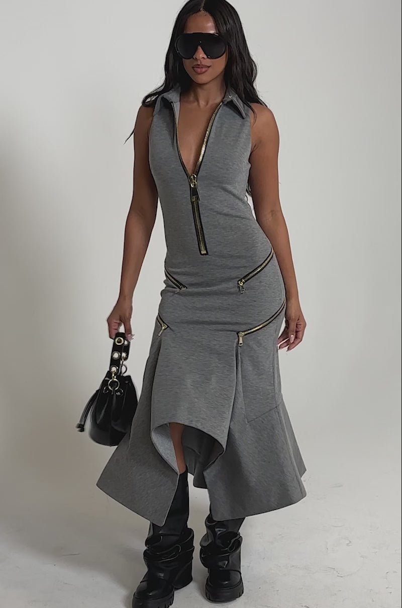 Video of woman modeling the ZIP CODE MAXI DRESS, a sleeveless heather-gray maxi with gold zippers. She pairs it with black knee-high boots, oversized black sunglasses, and a small black handbag