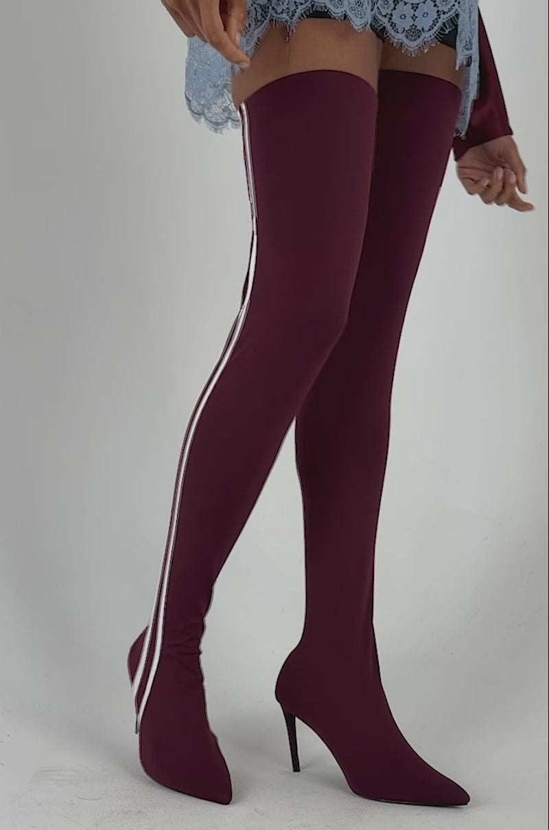 Video of a woman modeling the AZALEA WANG THALUNE BURGUNDY STRETCH SPORTY STILETTO boots—burgundy thigh-high boots featuring two white stripes and pointed high heels.