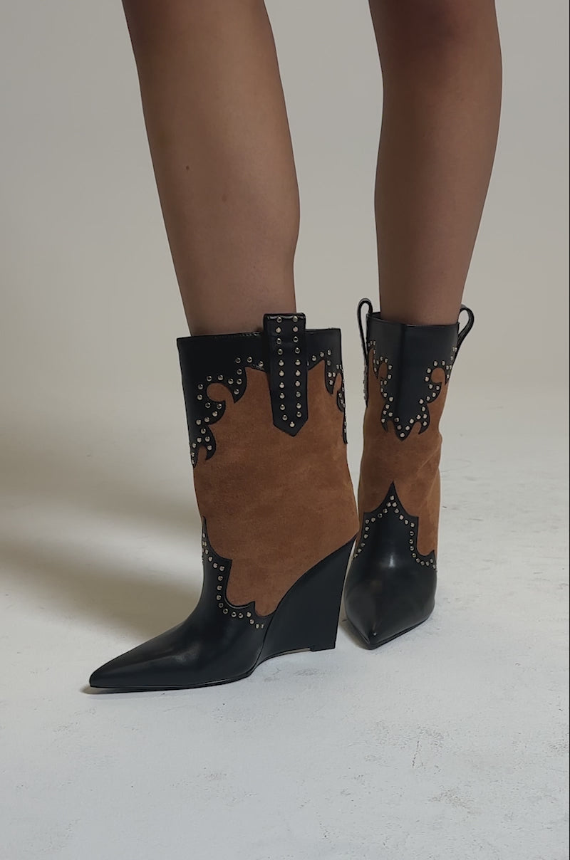A video of a person wearing the AZALEA WANG TALLULAH COGNAC WEDGE WESTERN BOOTIES with pointed toes and studded accents stands on a neutral background. Only the lower legs and boots are visible.