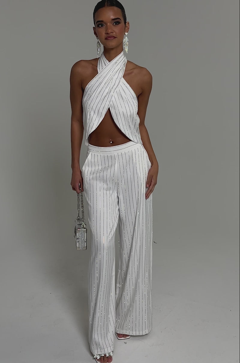 Video of woman modeling the PRINCESS TREATMENT RHINESTONE HALTER TOP, featuring a crisscross design and matching skirt. She accessorizes with dangling earrings and a belly button piercing, posing against a neutral background.