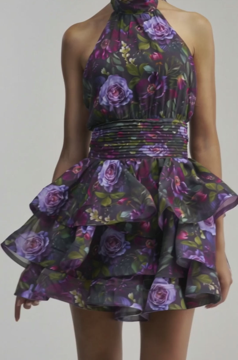 Video of a woman modeling the SPIN ME AROUND CHIFFON MINI DRESS IN BLACK MULTI—a sleeveless, halter-neck dress with layered ruffled tiers and a fitted waistband—she showcases an elegant silhouette. 