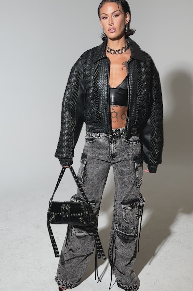 Video of woman modeling the KEEP IT LOWKEY PATCHWORK BOMBER—a black, textured leather jacket with woven accents—paired with gray acid-wash cargo jeans