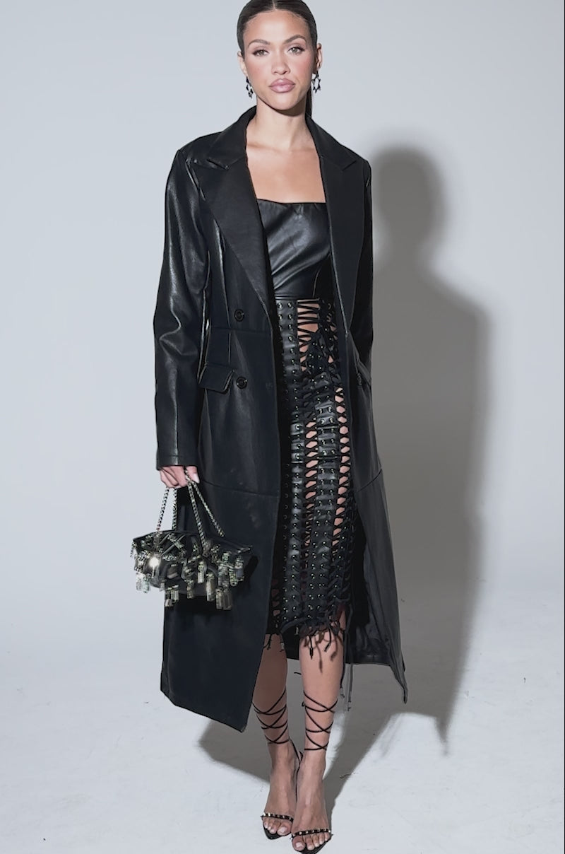 Video of woman modeling the EASY DOES IT FAUX LEATHER TRENCH over a strapless black top and a crisscross cutout skirt, styled with strappy high heels and hoop earrings.