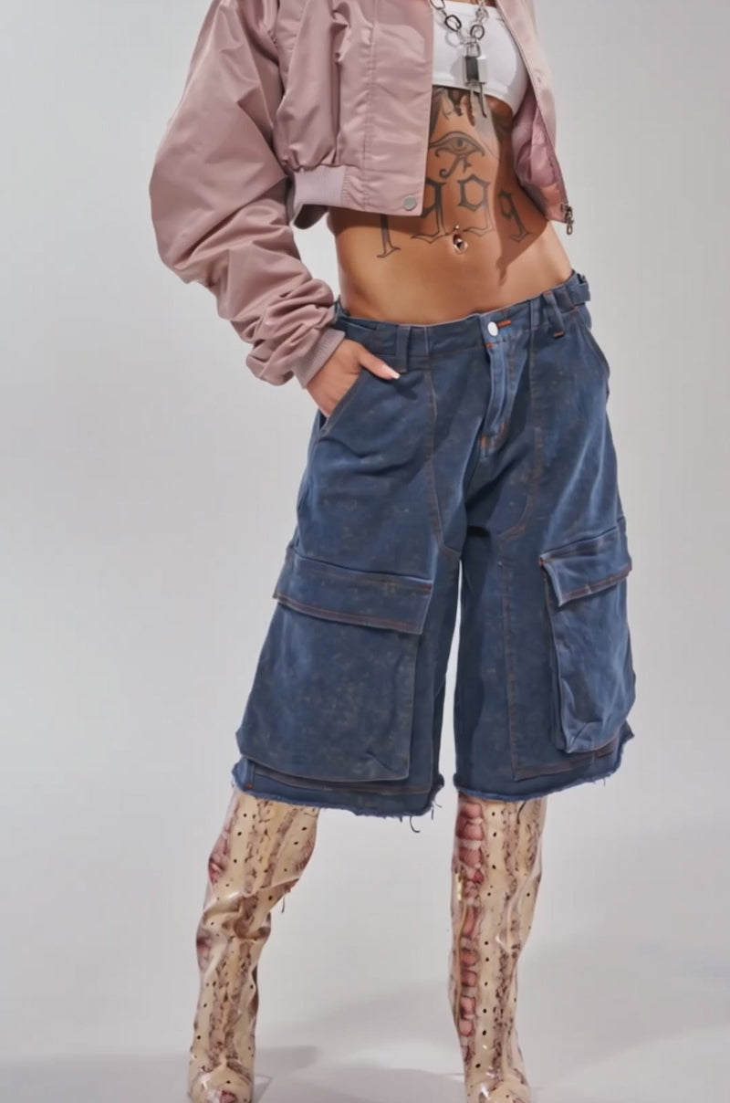 Video of woman modeling the TAKE IT EASY CROPPED BOMBER IN MAUVE with blue jeans, accessorized with hoop earrings, a belly button piercing, and a "1999" tattoo on her lower stomach. 