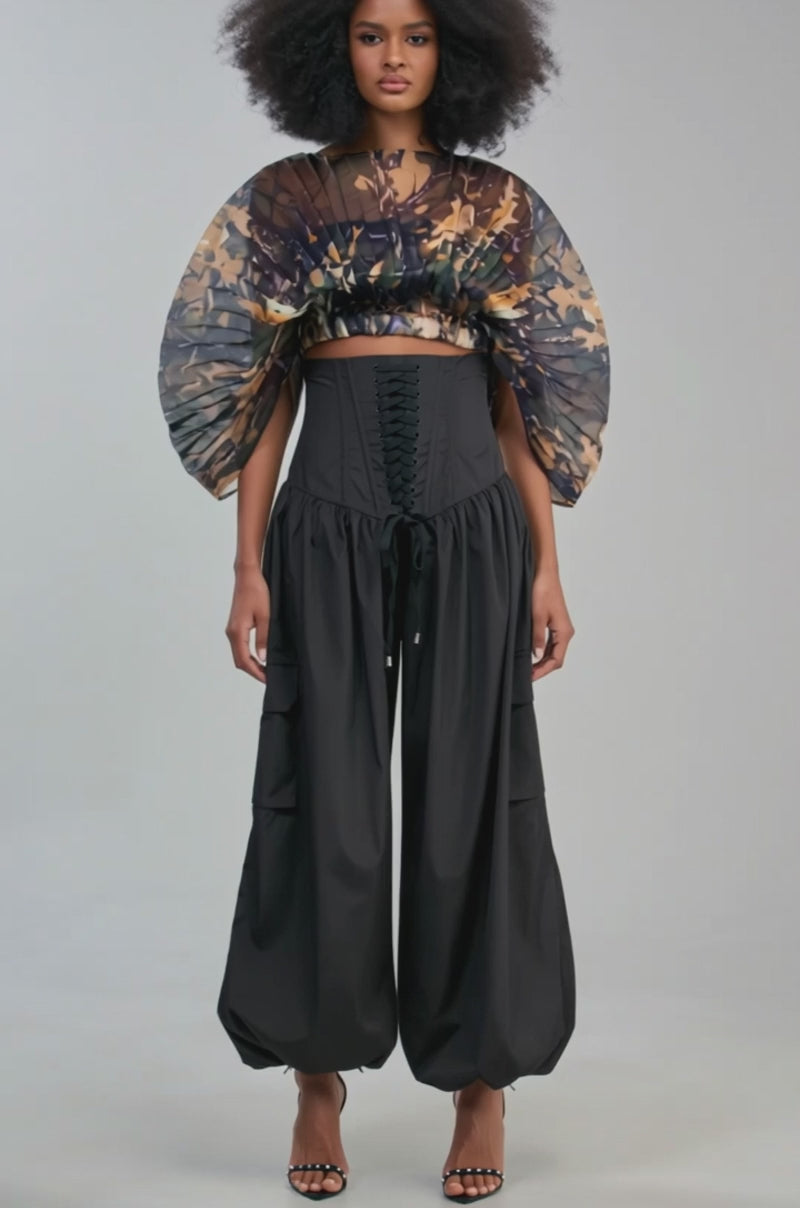Video of a woman modeling the LOCKED UP FOR GOOD BALLOON PANT IN BLACK, featuring black lace-up corset detail at the waist and wide, gathered legs reminiscent of balloon pants. 