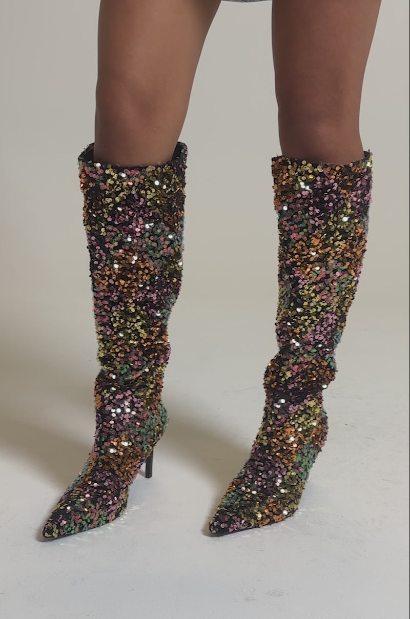 A video of a person wearing the AZALEA WANG JIMENA MULTI GOLD SEQUIN KNEE HIGH STILETTO BOOTS, covered in gold, purple, green, and orange sequins, against a plain light background.