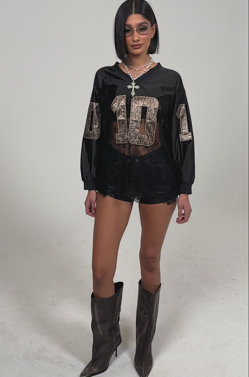 Video of woman modeling the ROCKY LACE JERSEY featuring "0101" in snakeskin print, and black lace shorts standing against a plain light background for a streetwear-ready look.