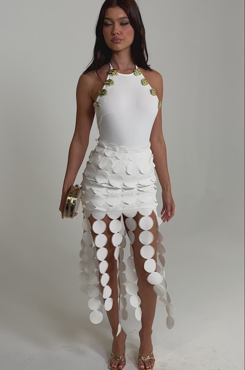 Video of woman modeling the LAKEN EMBELLISHED BODYSUIT, a white piece with gold seashell-accented straps 
