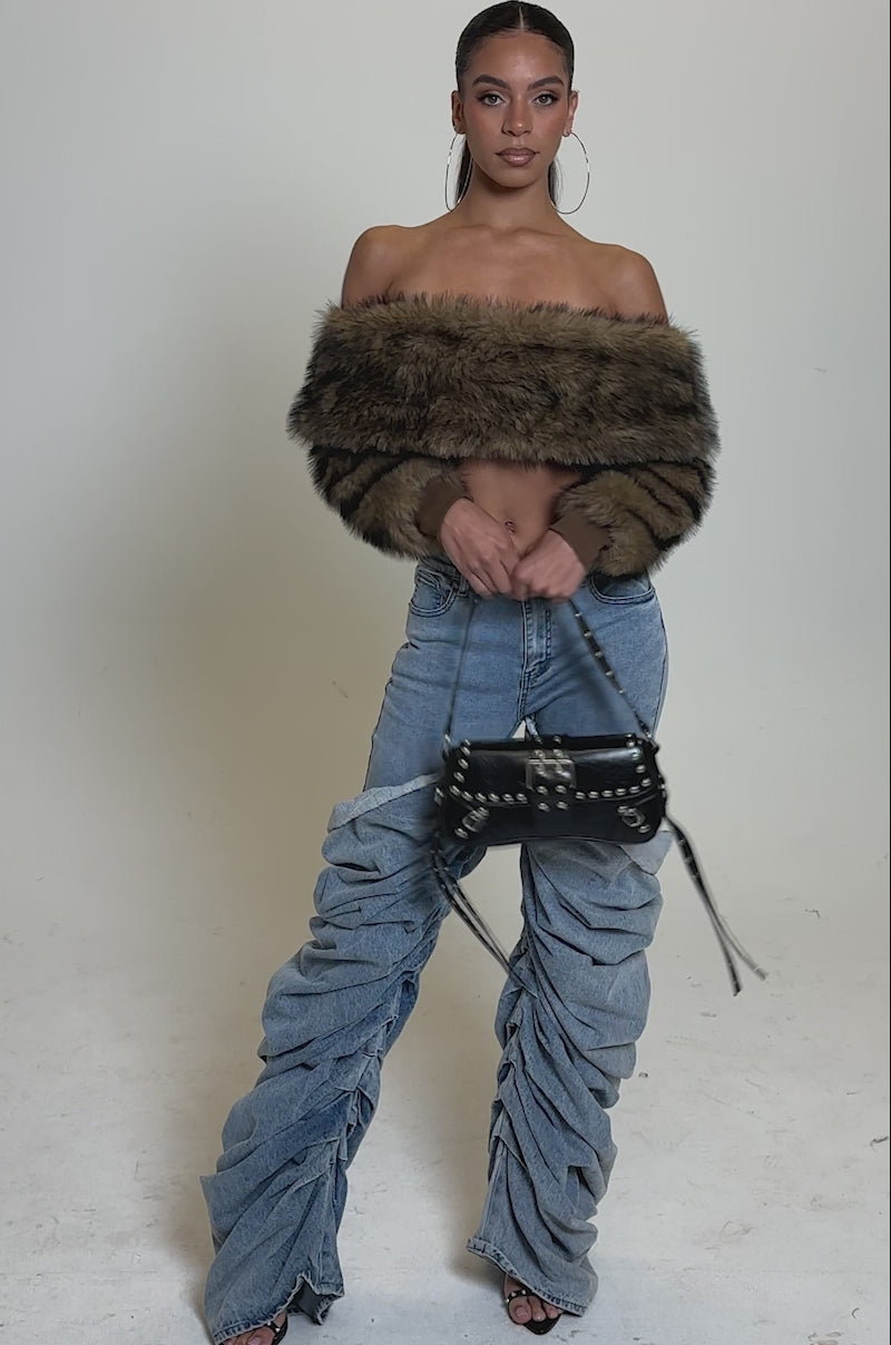 A video of a woman posing in the TEDDY BEAR CROPPED LONG SLEEVE TOP, ruched wide-legged jeans, hoop earrings, and a black studded handbag—a stylish winter look on a plain, well-lit background.