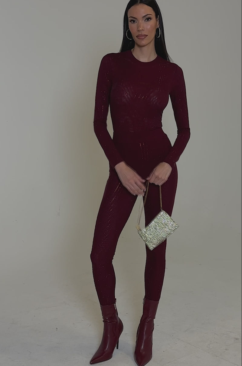Video of woman modeling the TWINKLING LIGHTS RHINESTONE LONG SLEEVE MESH BODYSUIT IN BURGUNDY, featuring subtle vertical shimmer stripes, against a light gray background while holding a gold strap in her left hand.