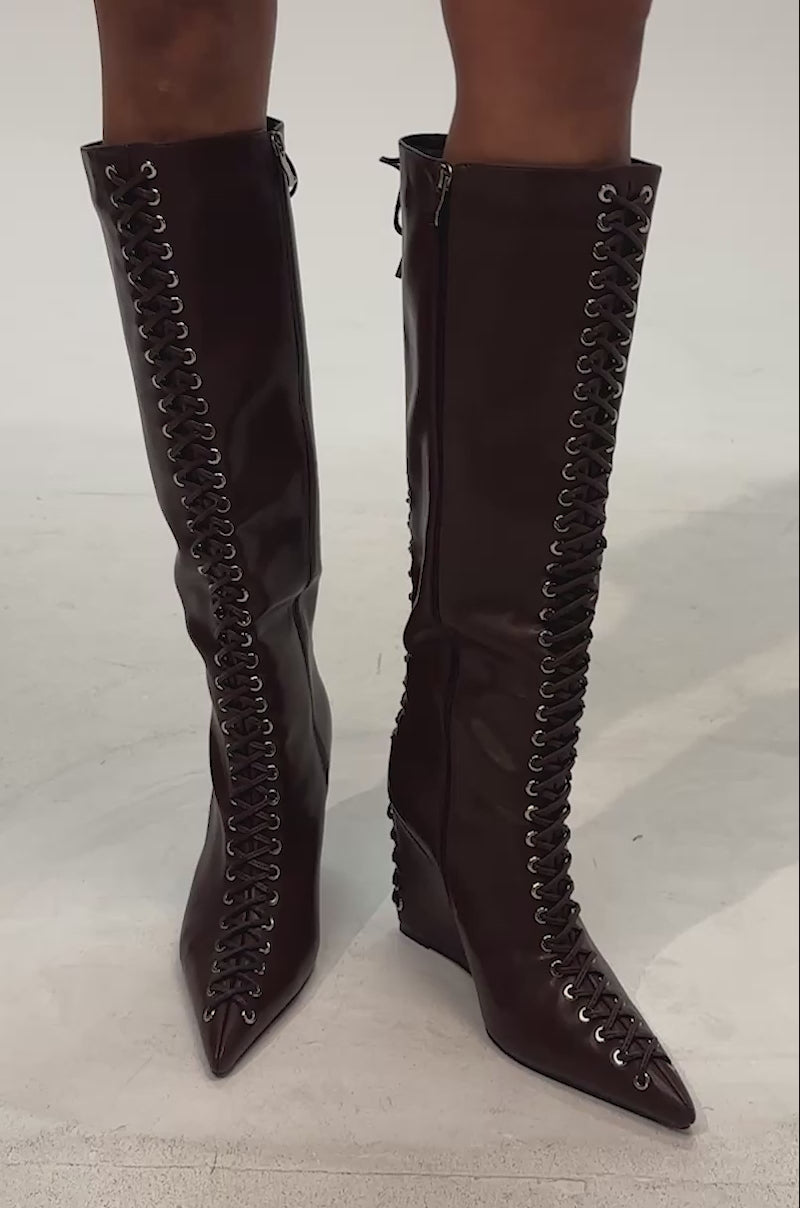 Video of woman modeling the AZALEA WANG THAUMUS BROWN LACE UP WEDGE BOOT—brown, knee-high wedge boots with silver eyelets and a side zipper
