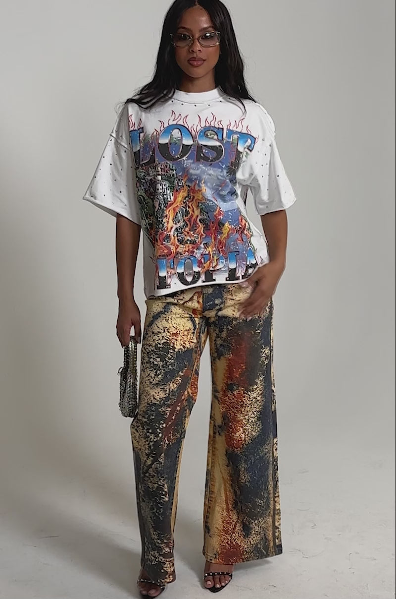 Video of woman modeling the POWER SQUAD RELAXED DENIM: high-rise, wide-leg denim pants with a bold abstract print in yellow, blue, red, and black, paired with open-toe black heels. 