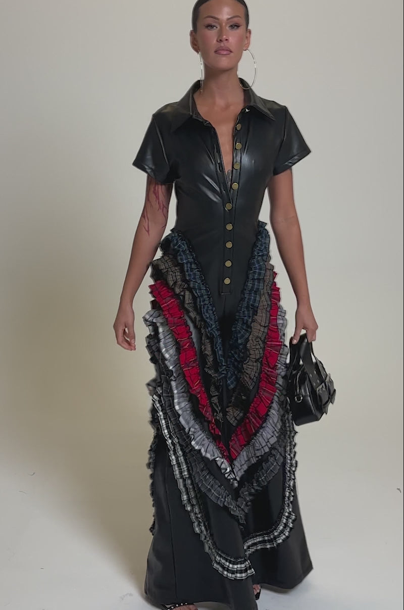 A video of a woman in the MAIN CHARACTER ENERGY PU JUMPSUIT, featuring short sleeves, gold buttons, and layered ruffled accents in red, blue, brown, and gray. 